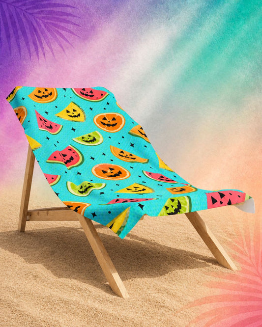 Summerween aesthetic beach towel with fruit jack o lantern design on beach chair, colorful spooky beach towel