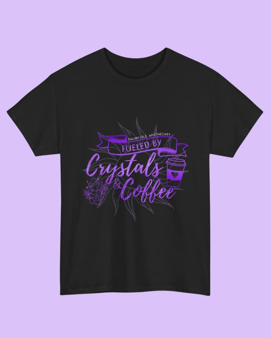 Flat lay of the black Fueled by Crystals and Coffee t-shirt highlighting the witchy graphic design and soft fabric on a dark background.