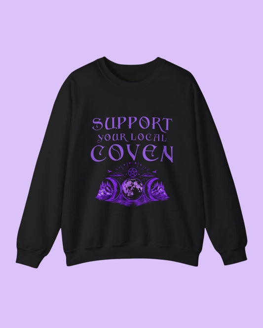 Flat lay of the Support Your Local Coven sweatshirt showcasing the witchy slogan design on a dark background, highlighting the cozy fabric and print detail.