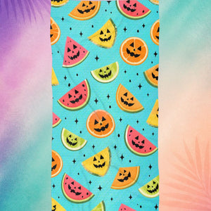 Summerween aesthetic beach towel with fruit jack o lantern pattern including watermelon, citrus, and pineapple, spooky summer vibe