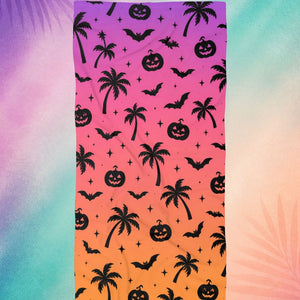 Summerween beach towel with palm trees, bats, and pumpkin pattern on pink and orange gradient, spooky beach aesthetic