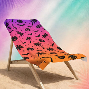 Summerween beach towel draped over beach chair with palm tree and pumpkin pattern, spooky summer beach aesthetic